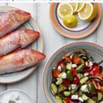 Fresh seafood feast with Greek salad, condiments, and seasonings on rustic wooden table.