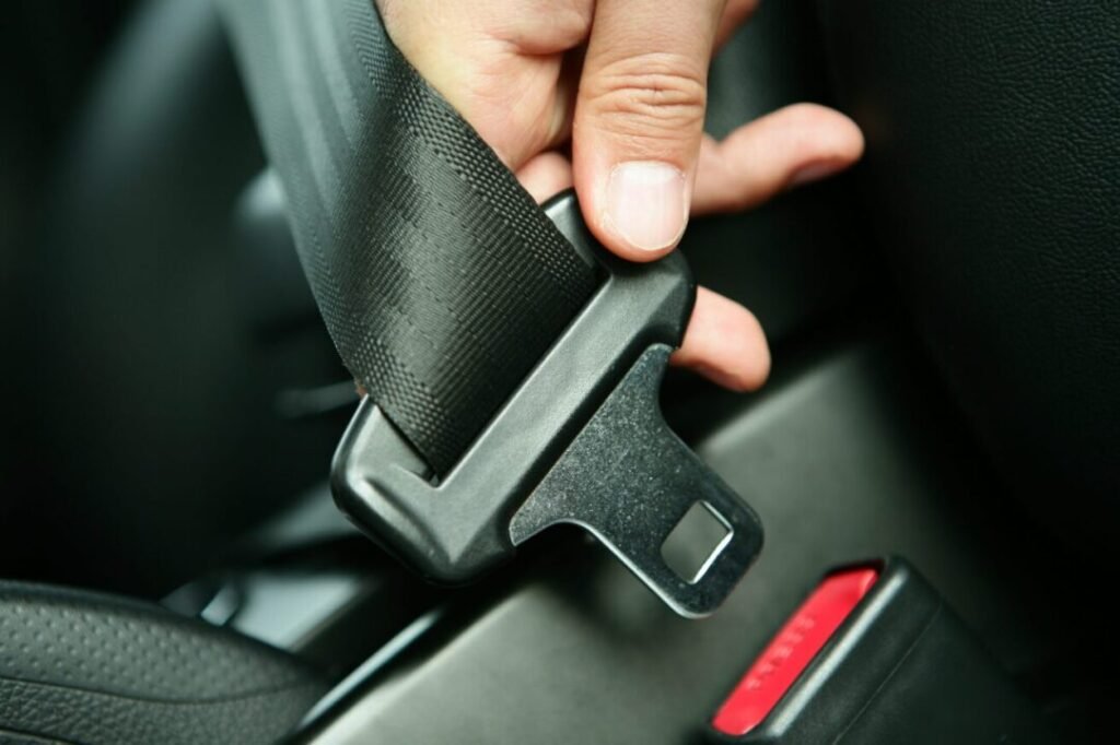 Close-up of a hand inserting a seat belt buckle in a car.