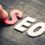 SEO concept: Hand arranging red and white letters on wooden surface for Search Engine Optimization.