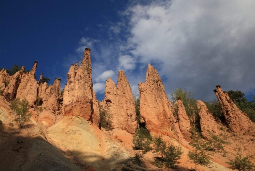 Tall, jagged red rock formations known as hoodoos under a vibrant blue sky with light clouds.