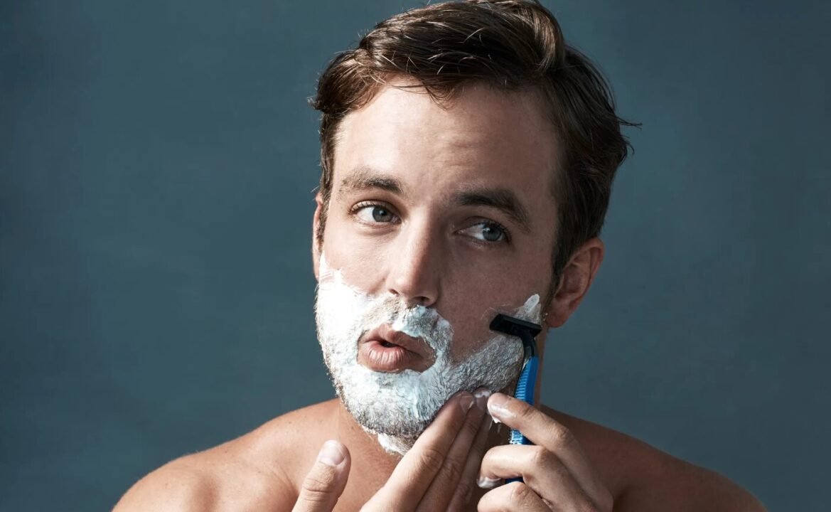 Man shaving with razor, focused expression, white foam on face.