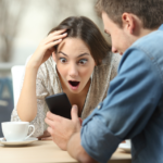 Man and woman sharing surprise on smartphone in cozy cafe.