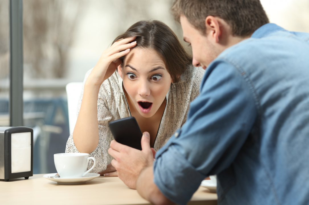 Man and woman sharing surprise on smartphone in cozy cafe.
