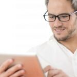 Man in white shirt uses tablet in well-lit room, showing modern, focused tech interaction.