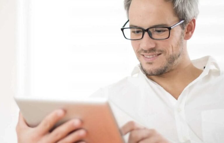 Man in white shirt uses tablet in well-lit room, showing modern, focused tech interaction.