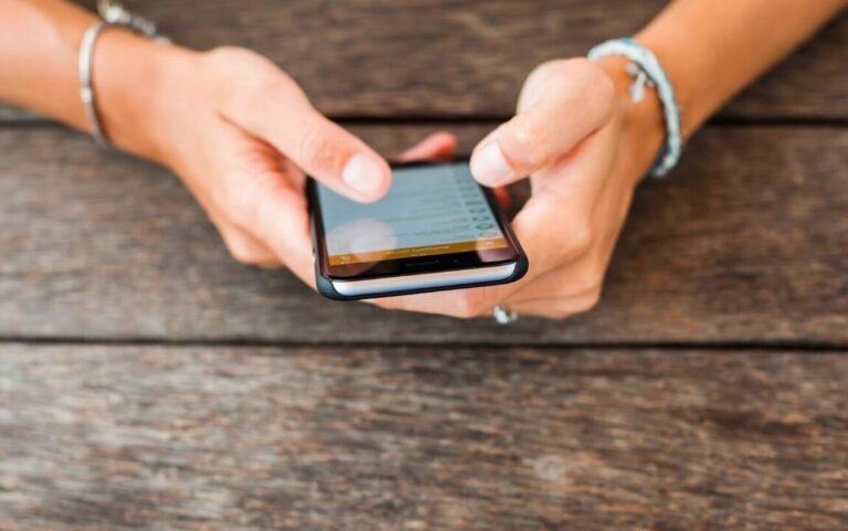 Persons hands using smartphone on wooden table, engaging with colorful screen content.