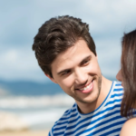 Man smiling happily at someone on a sunny beach day.