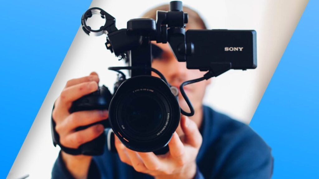 Person holding a Sony camera with various attachments, partially obscuring their face, against a two-tone blue and white background.