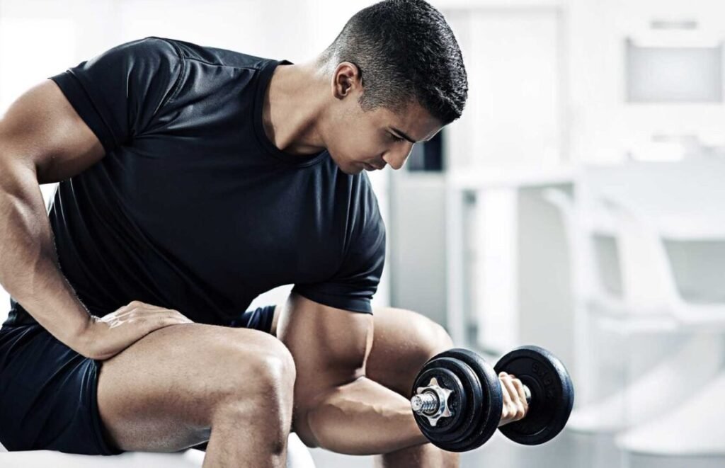 Man in black t-shirt lifting a dumbbell in a gym setting.