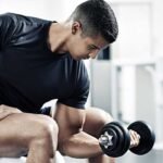 Focused man lifting dumbbell in modern gym, showcasing bicep curl exercise with determination.