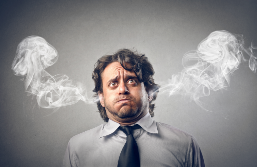 A man looking stressed with steam coming out from both ears against a gray background.