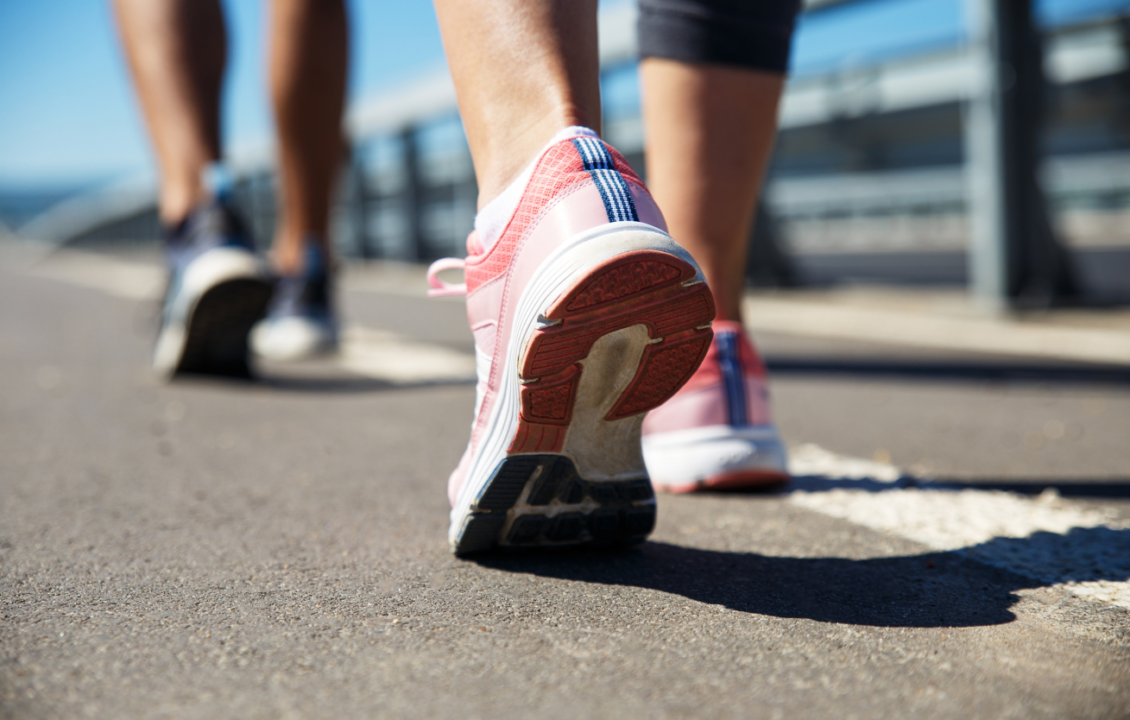 Two people walking in athletic shoes on a sunny day outdoors.