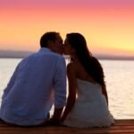 Tranquil sunset moment: couple on dock, colorful sky reflected in water, love and serenity.