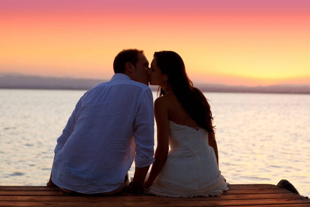 Tranquil sunset moment: couple on dock, colorful sky reflected in water, love and serenity.