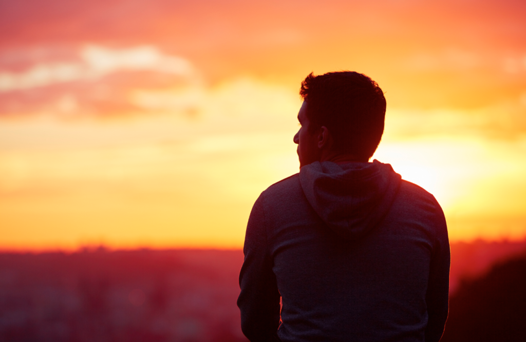 Silhouette of a person looking into the sunset with a vibrant orange and red sky in the background.