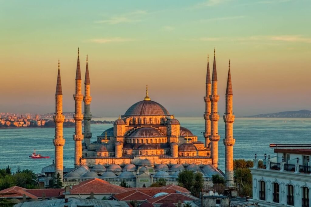 Sunset view of the Sultan Ahmed Mosque (Blue Mosque) in Istanbul, Turkey, with its minarets and large dome overlooking the Bosphorus and the distant city skyline.