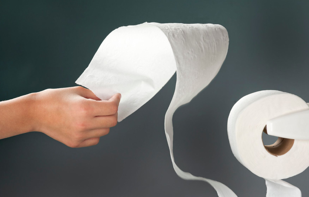 A person's hand pulling a sheet of toilet paper from a roll against a gray background.