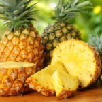 Ripe pineapples and juicy slices on wooden table in tropical setting.
