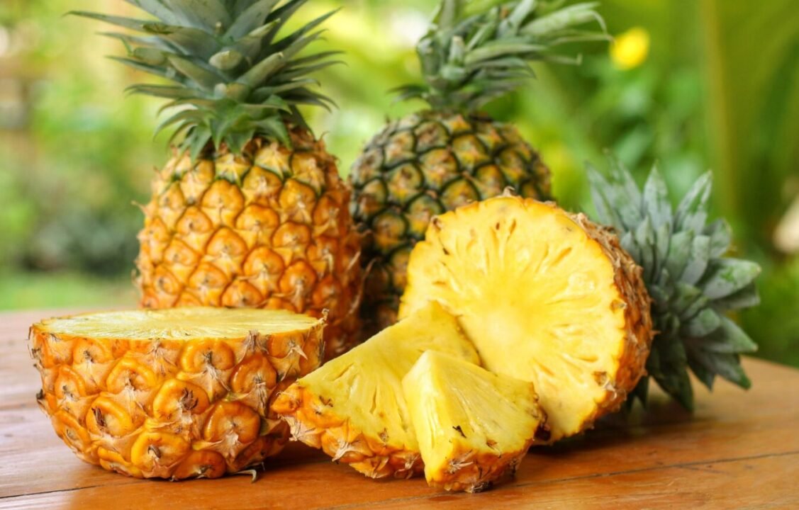 Ripe pineapples and juicy slices on wooden table in tropical setting.