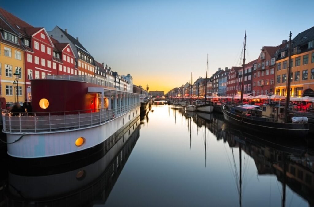 Twilight scene at Nyhavn with colorful traditional houses and boats reflecting in the calm water, Copenhagen, Denmark.