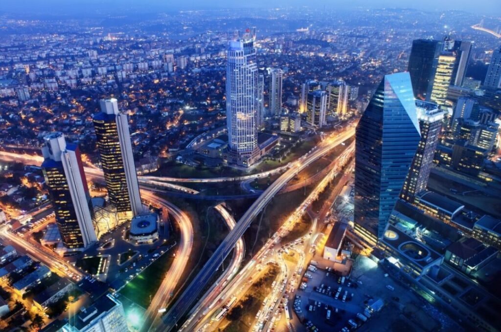 Aerial view of a bustling city at dusk, featuring illuminated skyscrapers, busy highways with light trails, and densely packed residential areas.