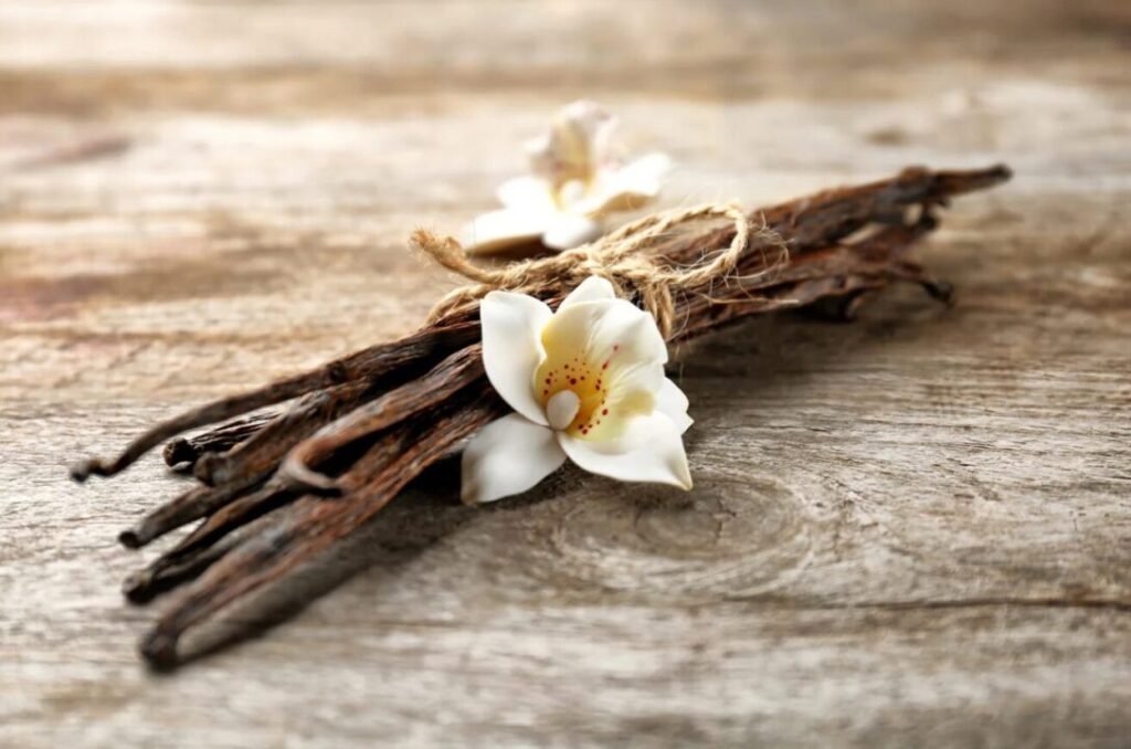 Vanilla pods tied with twine and white orchid flowers on a wooden surface.