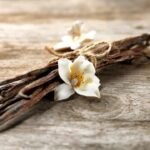 Rustic vanilla pods and white orchid flower on wooden surface for natural beauty.