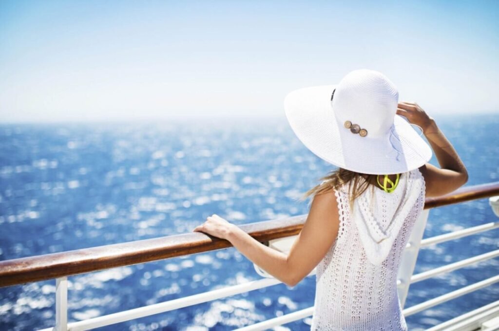 Woman in a white hat looking out over the sea from the deck of a ship.