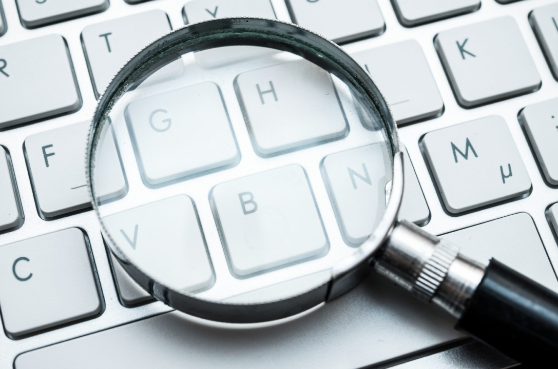 Close-up of white keyboard with magnifying glass on G key, symbolizing detailed digital examination.
