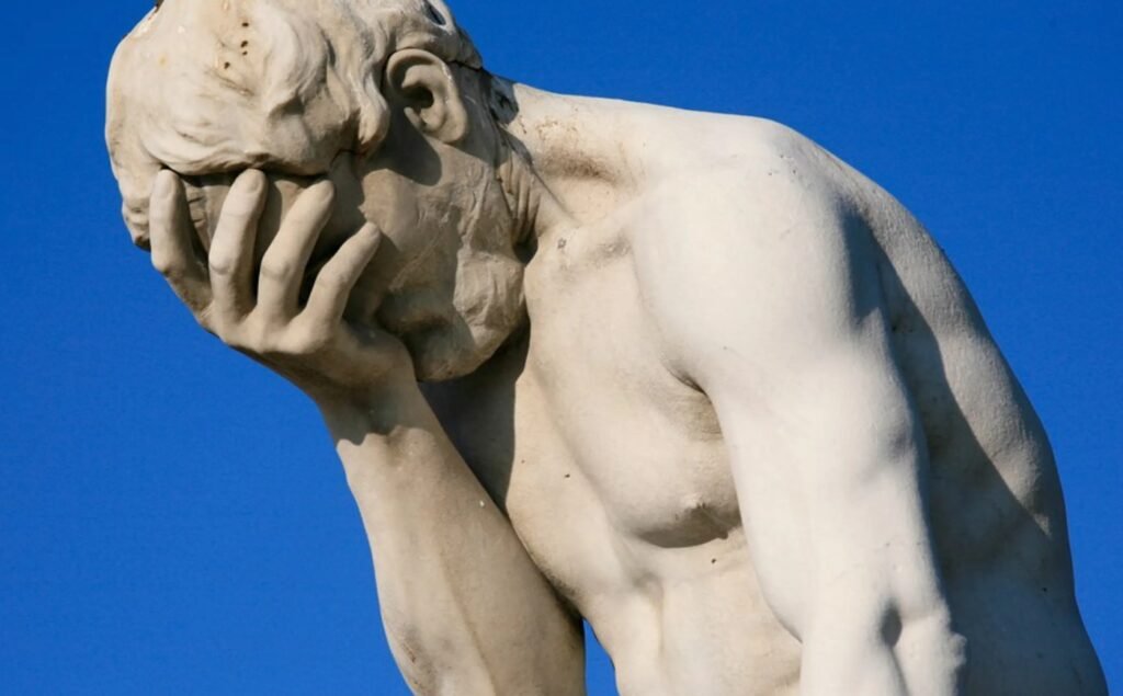 Sculpted male figure expressing grief against blue sky with exquisite detail and emotion.