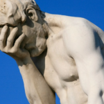 Sculpted male figure expressing grief against blue sky with exquisite detail and emotion.