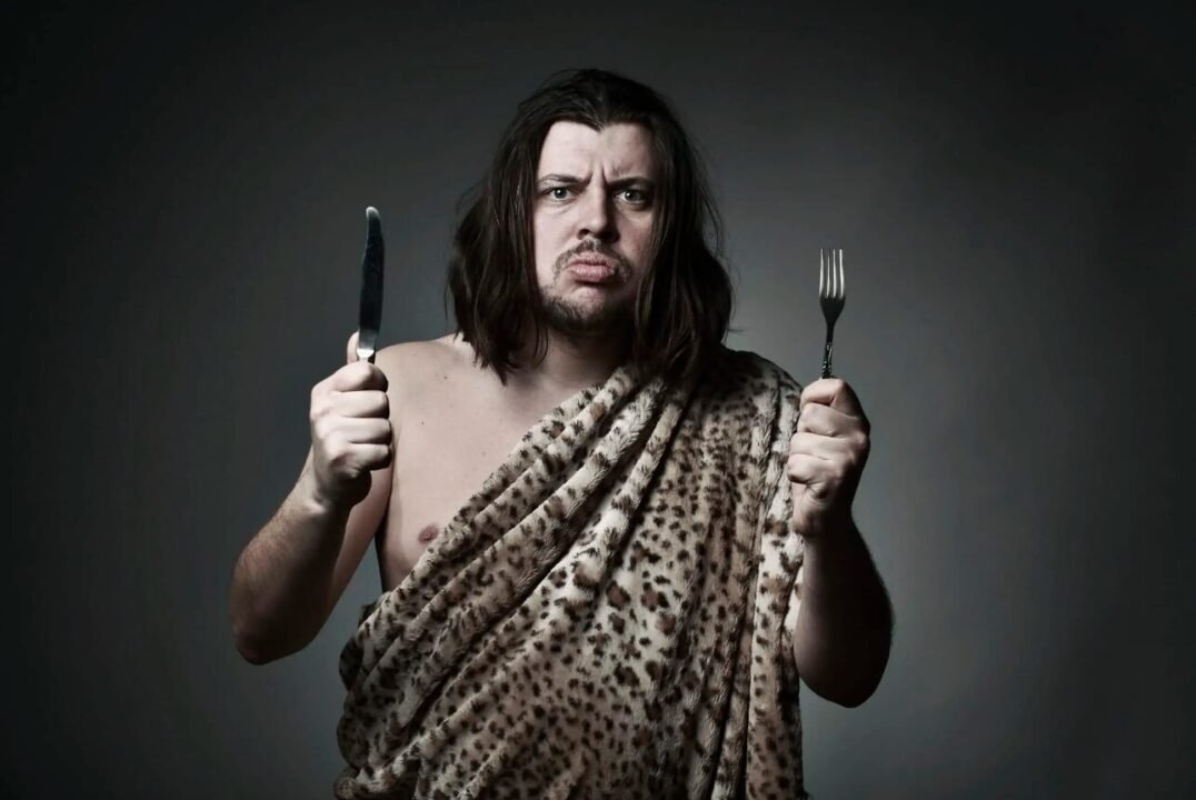 Wild hunter in animal print with knife and fork in comical mealtime standoff.