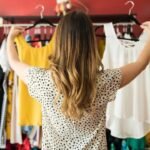Woman comparing yellow and white tops in vibrant clothing boutique.