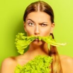 Young woman playfully posing with lettuce mustache in vibrant green setting.