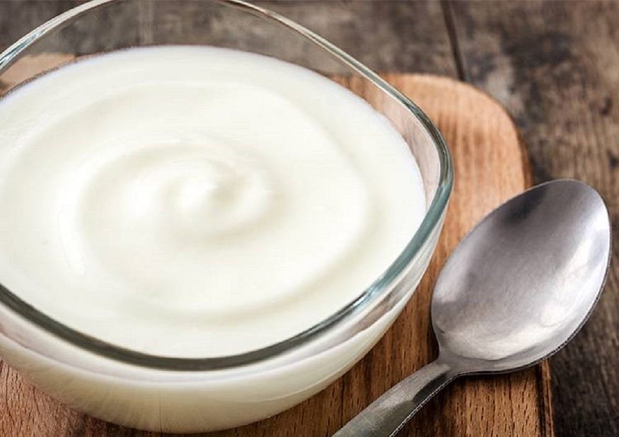 A bowl of yoghurt on a wooden board with a spoon to the side.