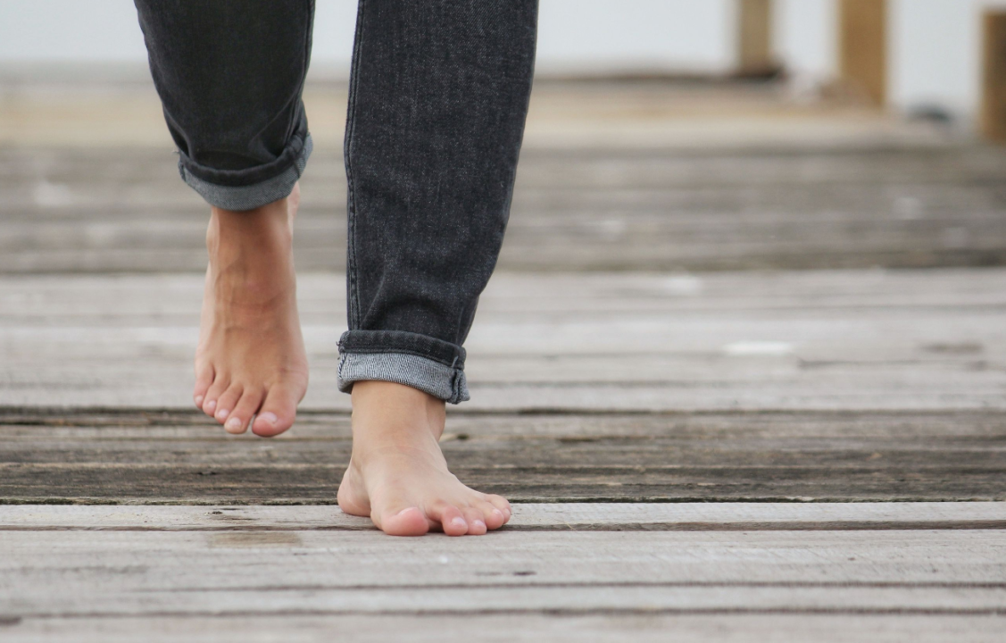 Casual stroll on wooden boardwalk, bare feet in rolled-up jeans.