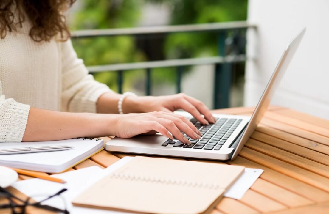 Serene outdoor workstation with laptop, notepad, and greenery creating a focused work environment.