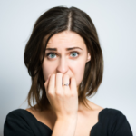 Anxious young woman biting nails, expressing worry and distress against neutral gray backdrop.