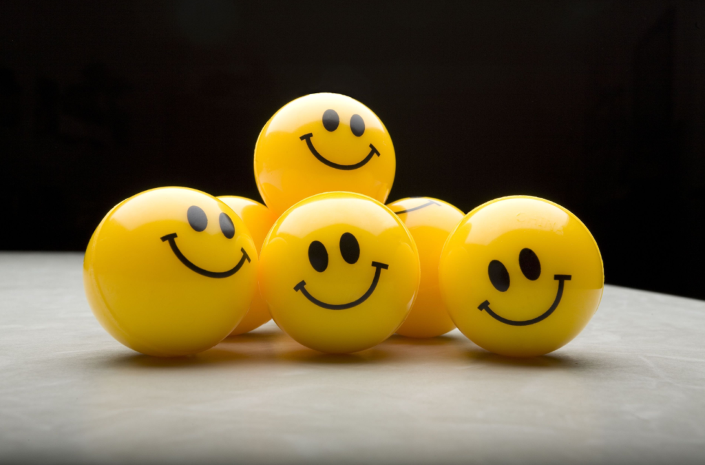 Five yellow balls with smiley faces arranged on a surface, against a dark background.