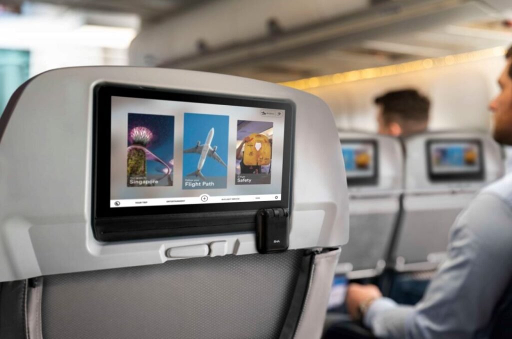 Passenger viewing an in-flight entertainment screen showcasing options like images of Singapore, a flight path, and safety guide on an airplane.