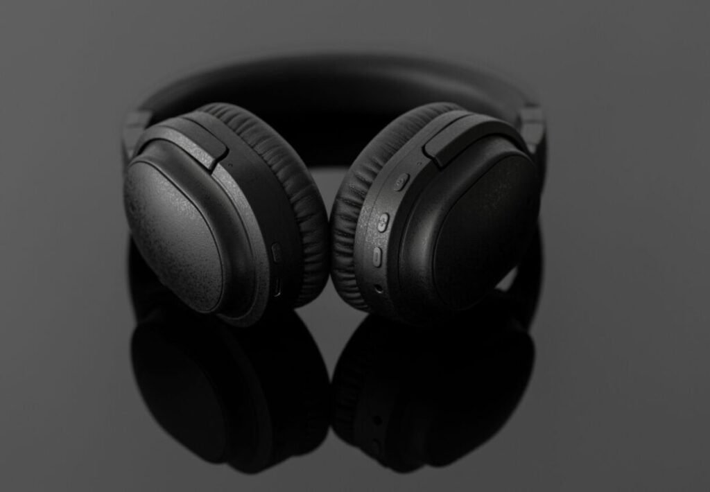 Black wireless headphones with textured details, displayed against a grey background with a reflective surface.