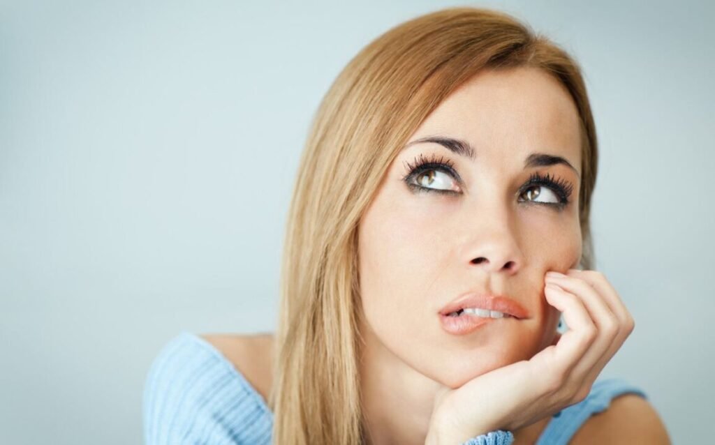 Woman with long blonde hair looking up with a contemplative expression.