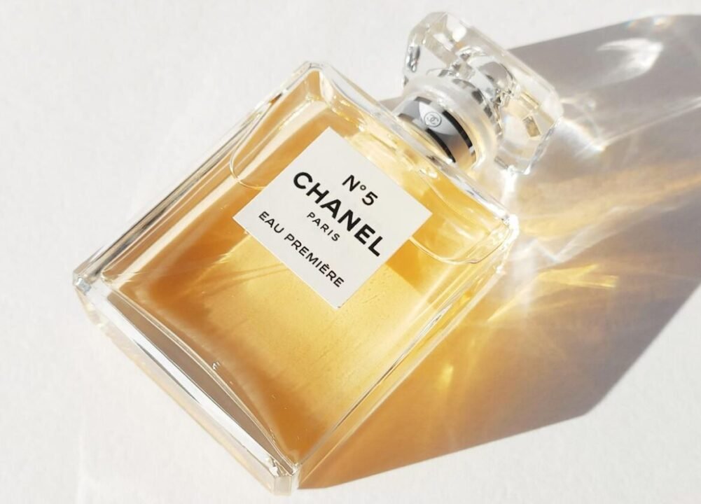 A bottle of Chanel No. 5 Eau Premiere perfume, with a clear glass design and a square label, sitting on a white surface with sunlight casting shadows.