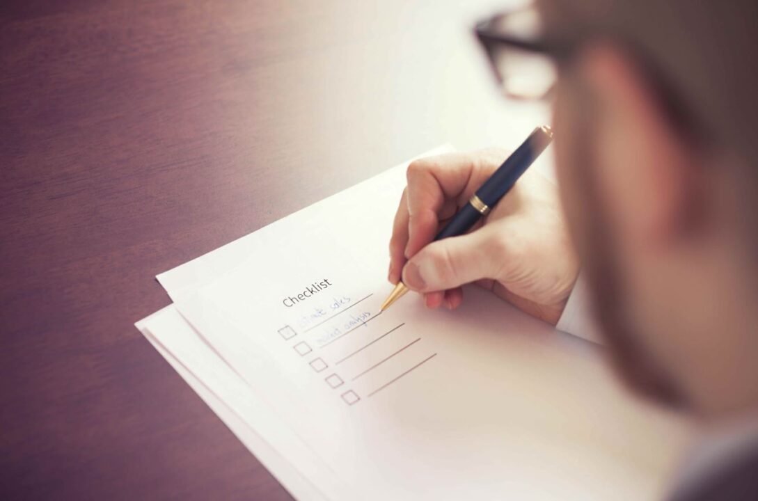 A person filling out a checklist with a pen on a wooden table.