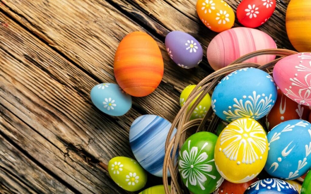 Colorful painted Easter eggs with floral patterns, some spilling from a wicker basket onto a rustic wooden surface.