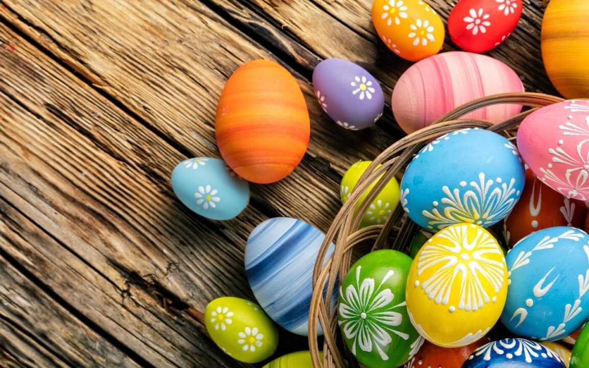 Colorful painted Easter eggs with floral patterns, some spilling from a wicker basket onto a rustic wooden surface.