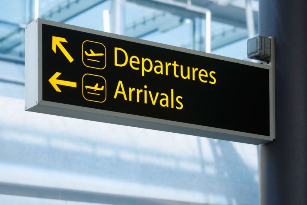 Airport sign guides travelers to departures and arrivals with elevator and suitcase symbols.