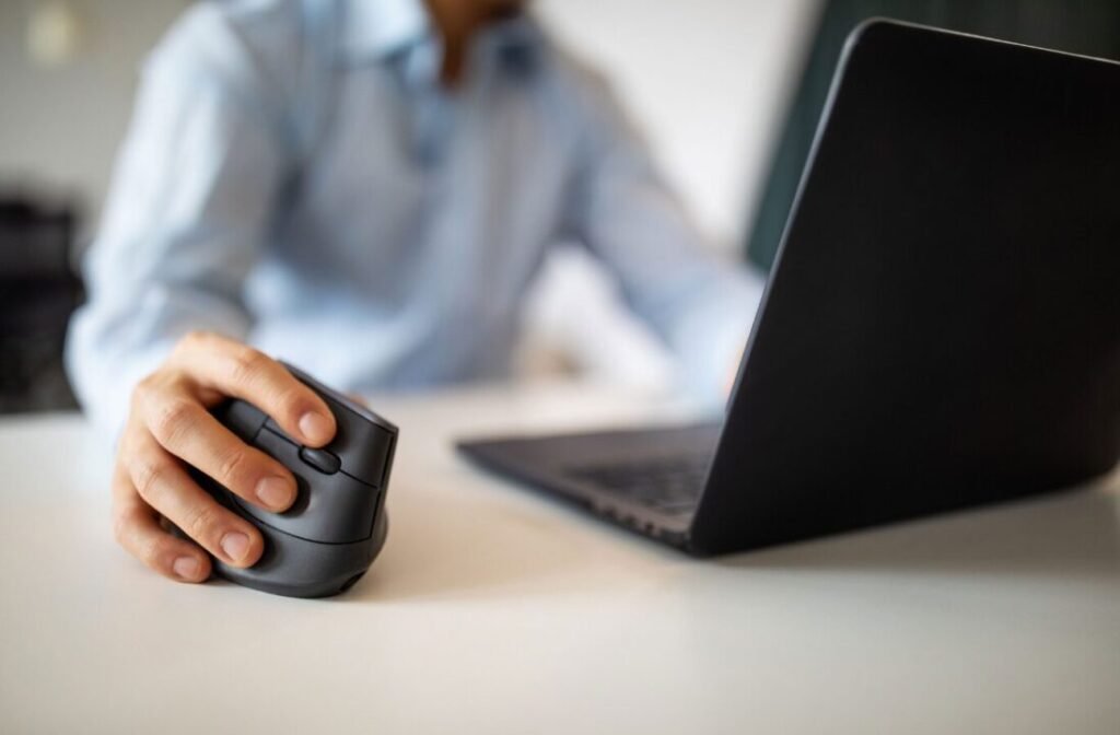 Person using an ergonomic vertical mouse while working on a laptop in an office setting.