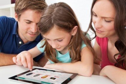 A man, a woman, and a young girl are sitting together, looking at a tablet. The girl is using her finger to navigate the screen while the adults attentively watch.