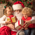 Santa gives gifts to children in cozy Christmas scene with festive decorations.